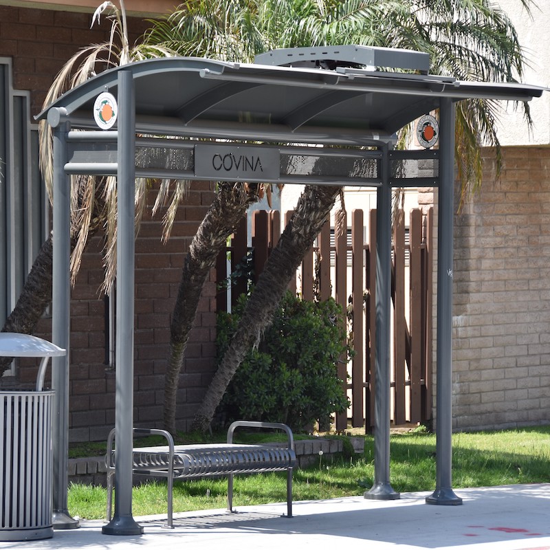 Bus shelter in Covina, CA with a bench with no backing and a trash receptacle on the outside left side