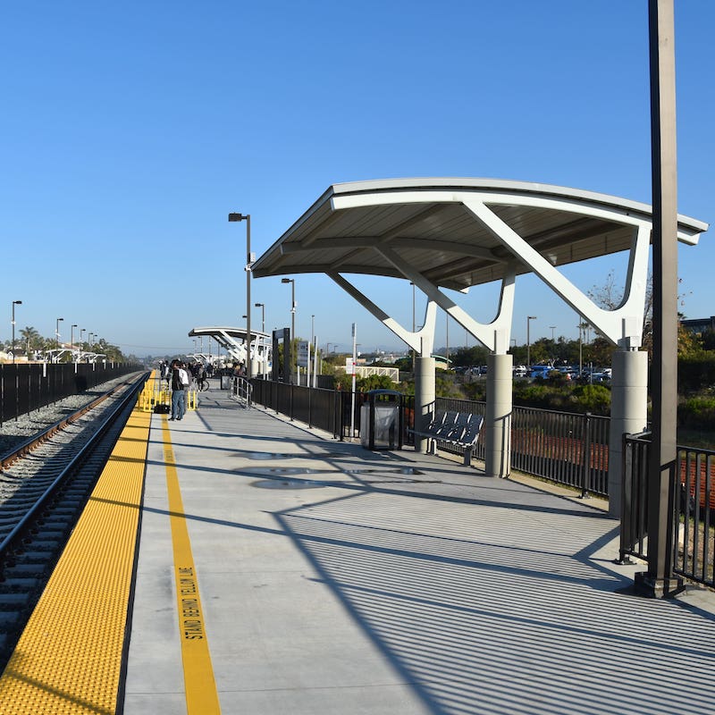 A transit station is seen with multiple shelters with bench seating and trash receptacles alongside the track