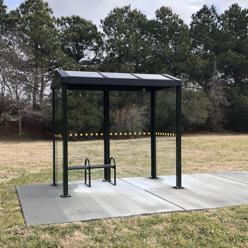 A bus shelter from the front with a bench on the left inside with seating for two. Glass paneling with a subtle yellow dot design around the middle of the panels.