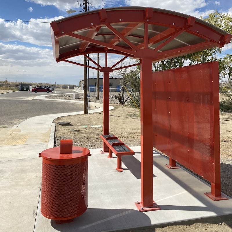 A signa voyager bus shelter is seen with a custom burnt orange color on the shelter, the trash receptacle and the bench for three.