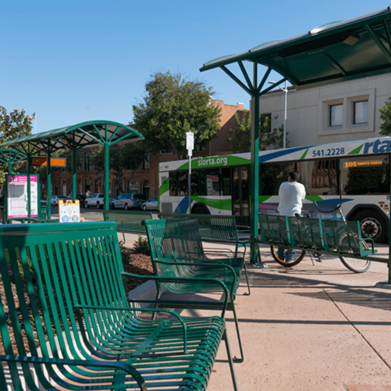 Two benches on the left with a rider and their bike awaiting the bus to open its doors.