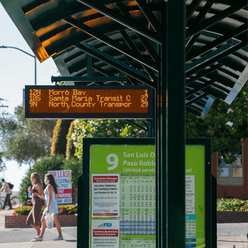 A transit center shelter displays rider information as well as a digital board on the top of the shelter with times until the next bus arrives.