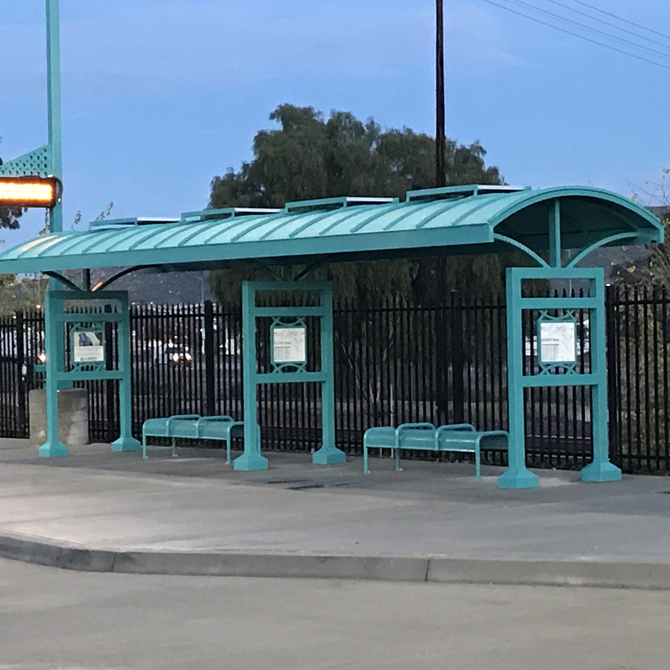 Two bus shelters next to one another with bench seating under each with rider information displayed on each post.