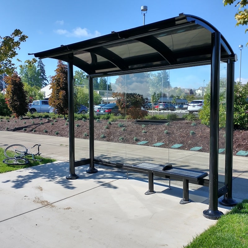 A bus shelter with glass paneling on the back and sides and a bench with seating for two inside the shelter.