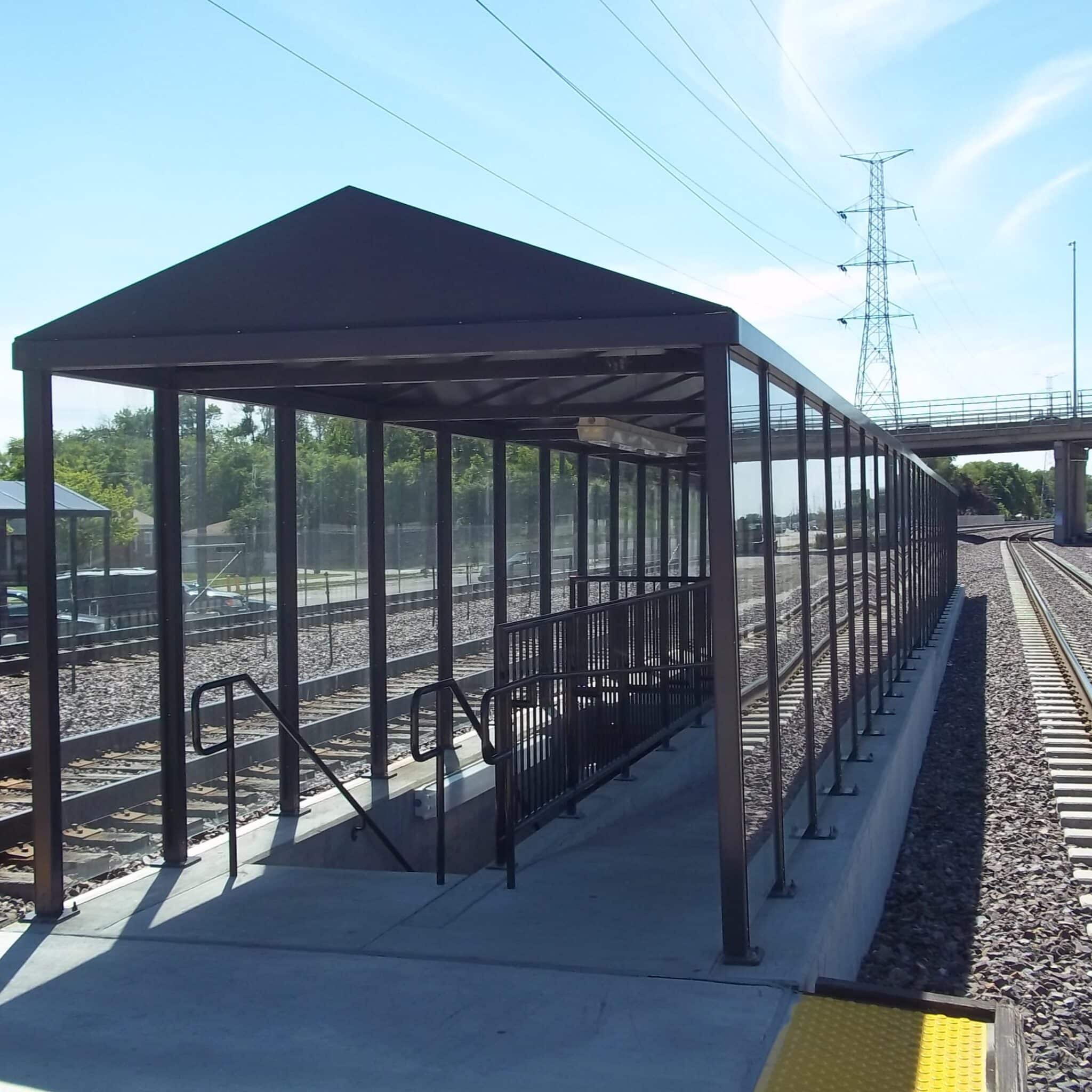 A transit shelter covers a walkway and staircase between two sets of metro tracks.