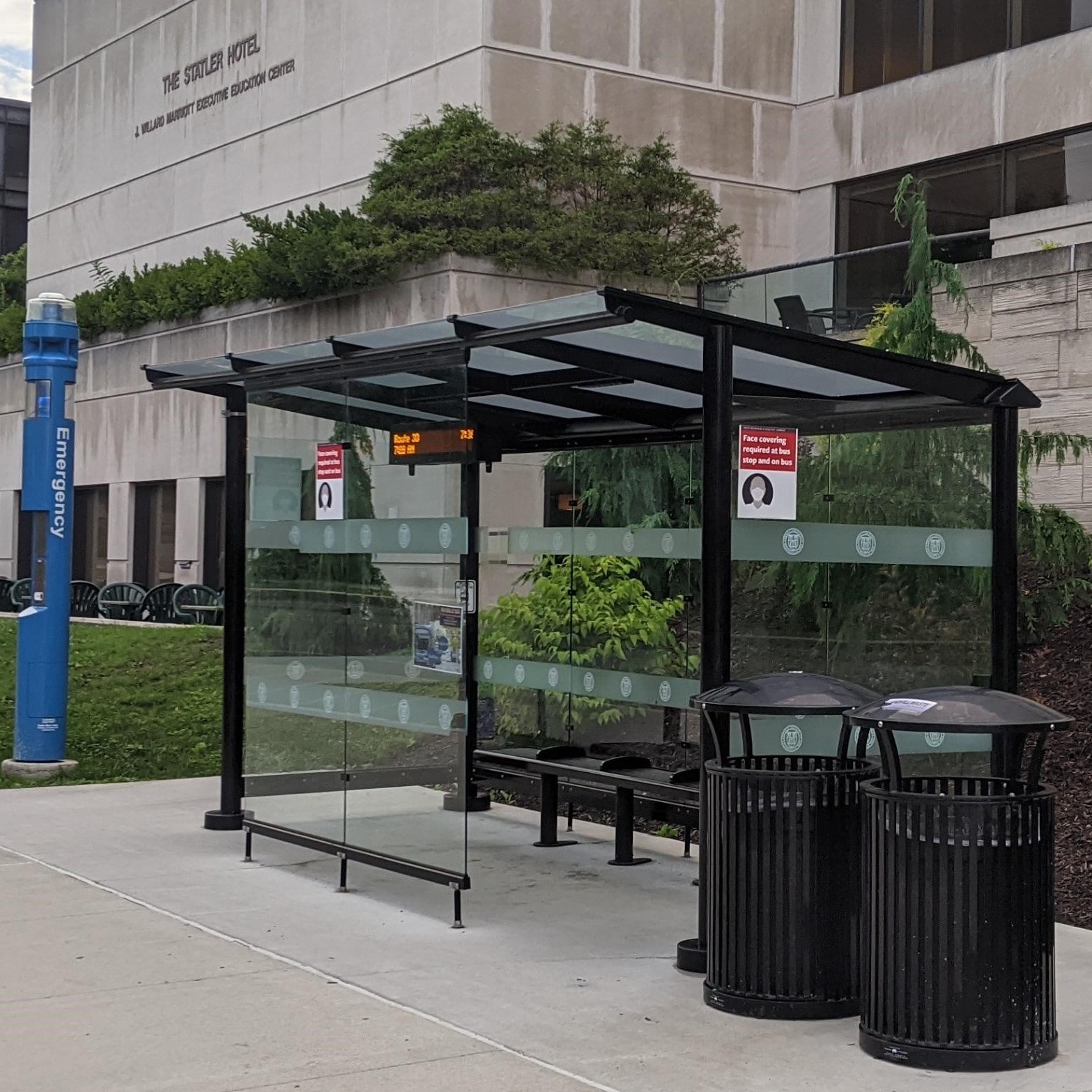 Cornell left side view of a bus shelter with custom Cornell logo stripes with bench seating inside and two trash receptacles outside