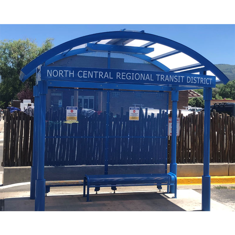 A bus shelter for North Central Regional Transit District is seen from the front with rider information displayed on the back panels and bench seating.