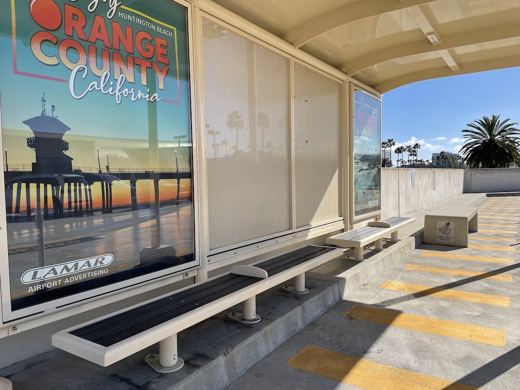 A left side view of a bus shelter with advertising displays on the back panels and bench seating inside and out.