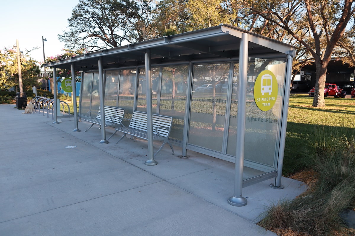 A bus shelter in St. Pete Pier is seen with two benches and on the left, bike hoops for bike parking.