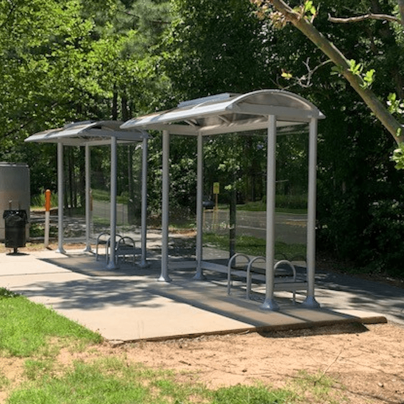 Two bus shelters sit side by side on a slab of cement with bench seating under both.