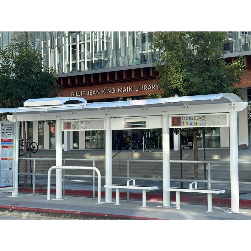 A siga custom bus shelter is seen from the front with a rider information display on the left, a bike stand and two benches for rider seating.