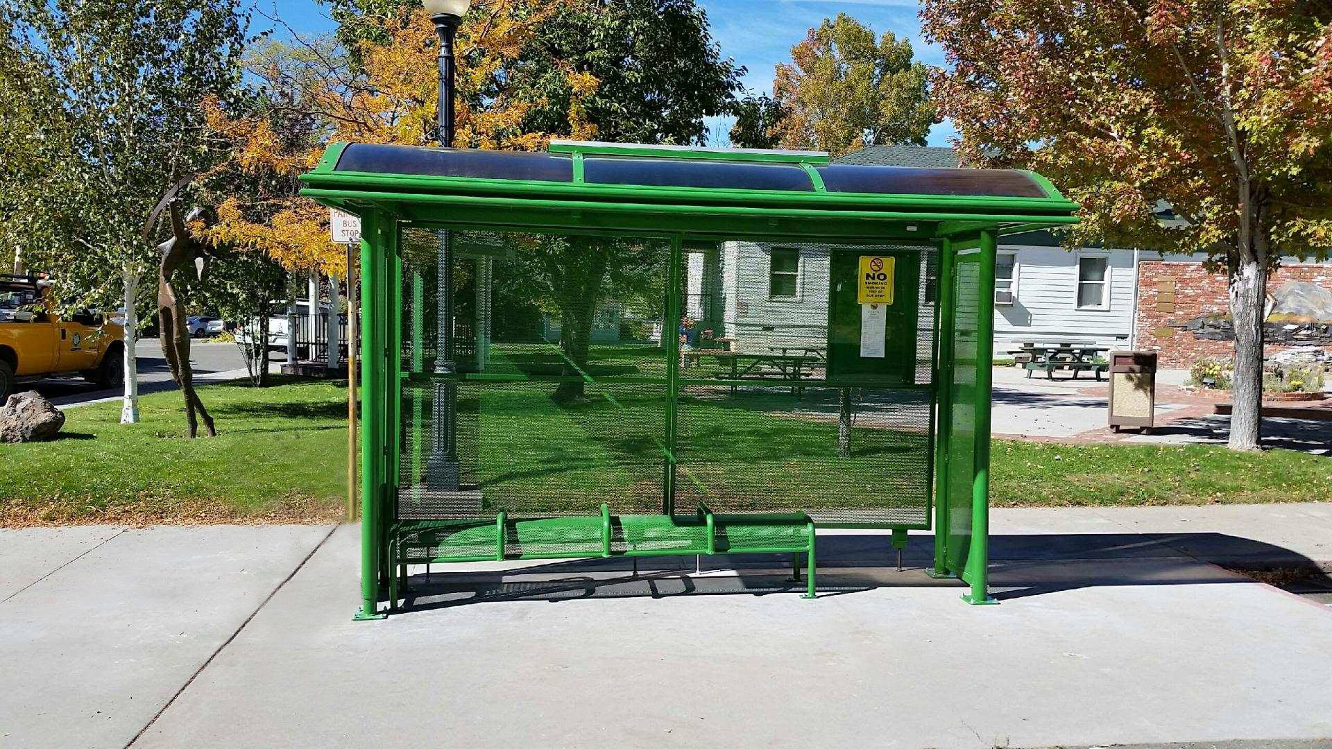 A sierra series bus shelter is seen from the front with a bench seating for four and a rider information display on the back right panel.