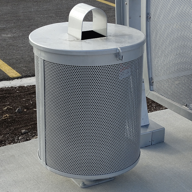 A silver trash receptacle with a covered top with a small opening with an arched cover on top to minimize things other than trash going inside.
