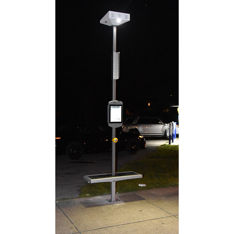 A bus stop post with bench seating attached and a light at the top seen at night.