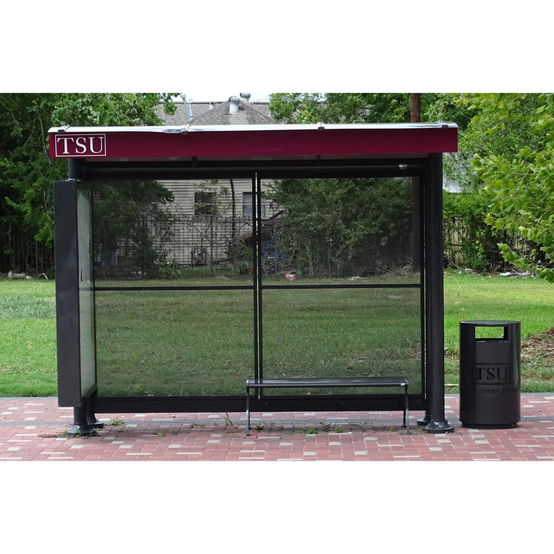 A siga sunset bus shelter is seen from the front outside TSU with a left side panel display, bench seating and a trash receptacle on the outside right.