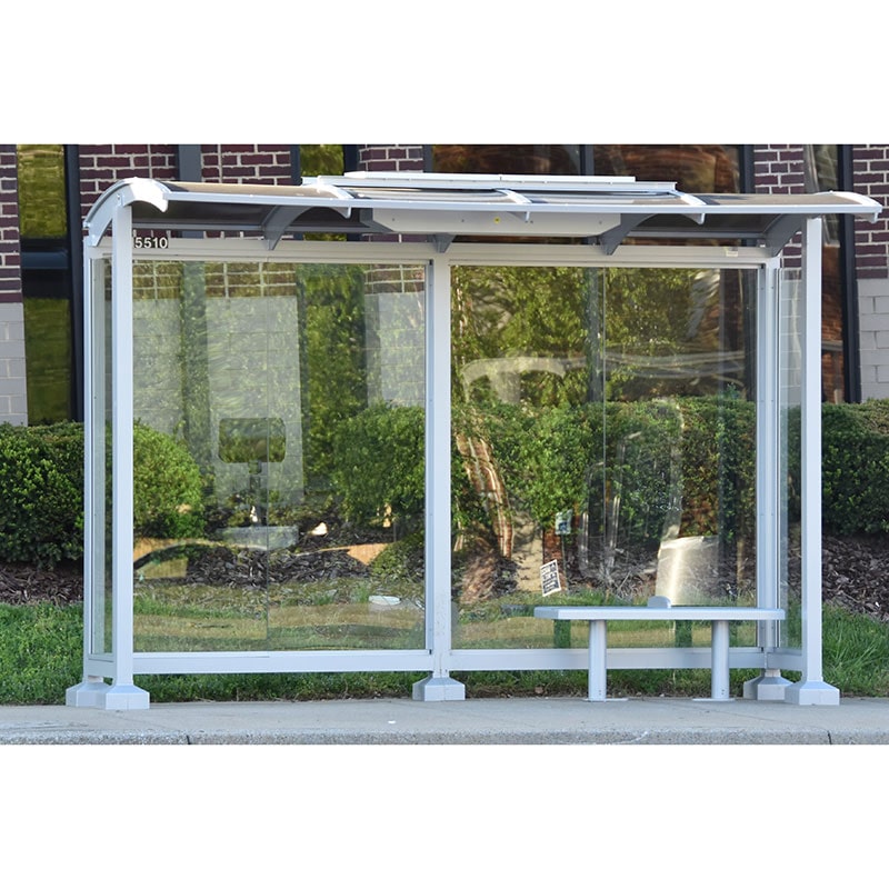 A signa sunset bus shelter is seen from the front with glass panel siding and a bench for two riders.