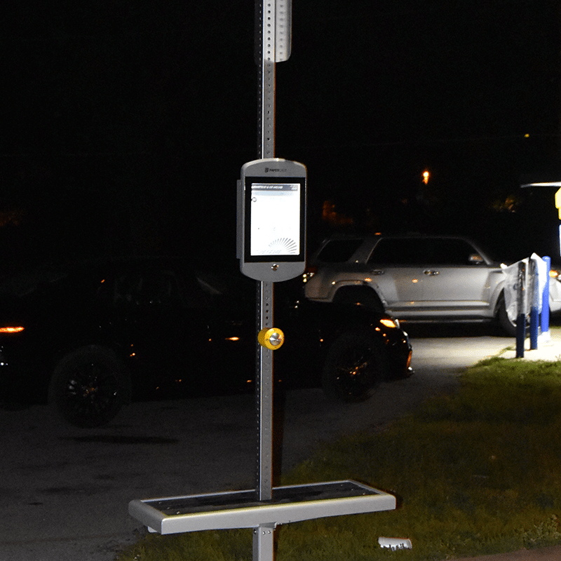 The bottle half of a bus shelter post is shown at night from the front with seating on both sides of the post, rider information attached to the post and lighting overhead.