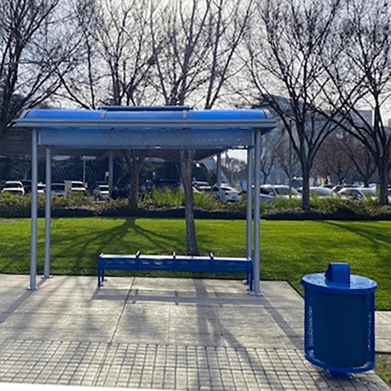 A bus shelter is seen from the front with bench seating inside the shelter and a trash receptacle on the outside right.
