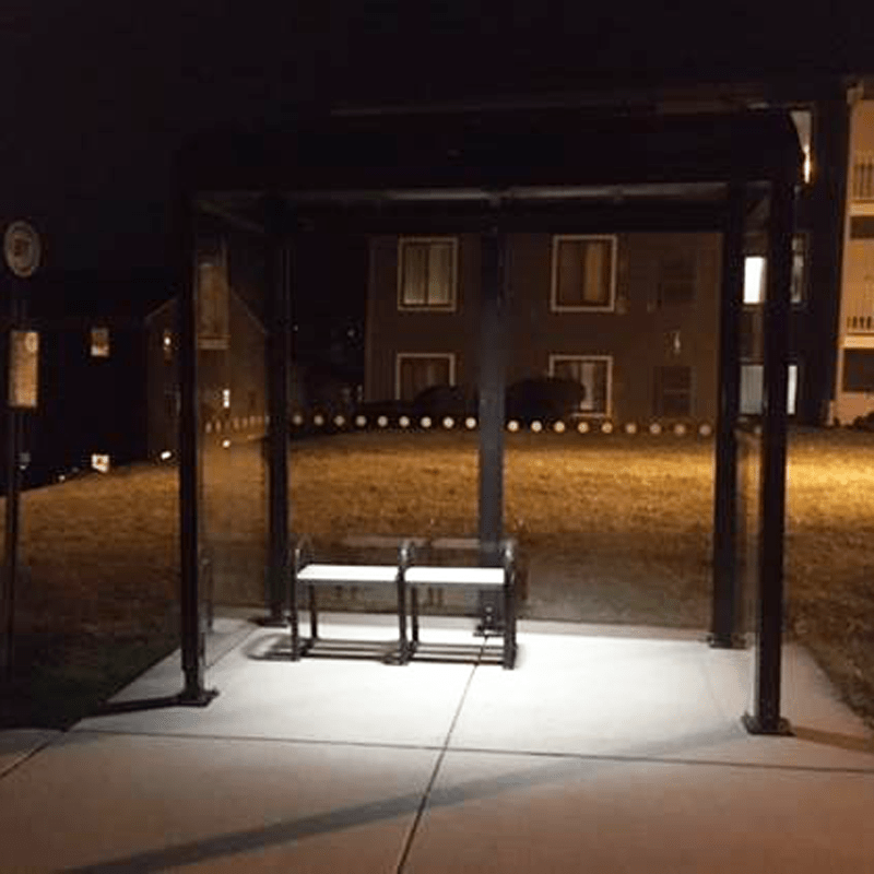 A bus shelter is seen at night from the front with bench seating inside the shelter at night.