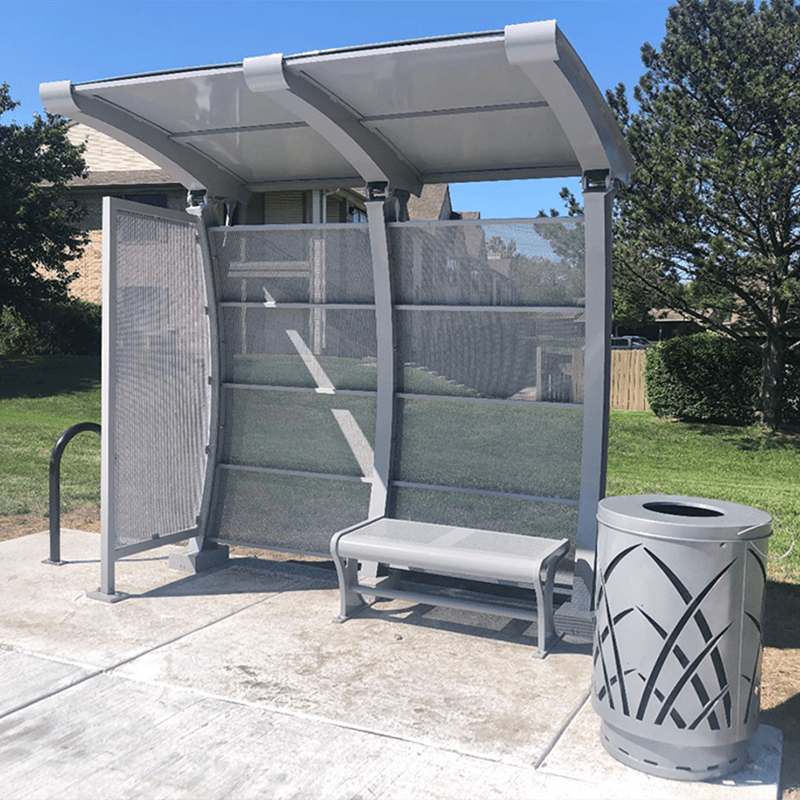 A signa crescent bus shelter is seen from the front with bench seating, an arched structure design and a right side trash receptacle.