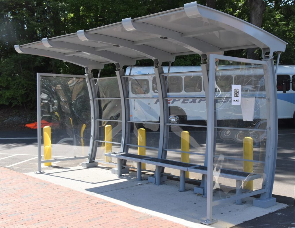 Long three bench piece under a crescent bus shelter with glass sides