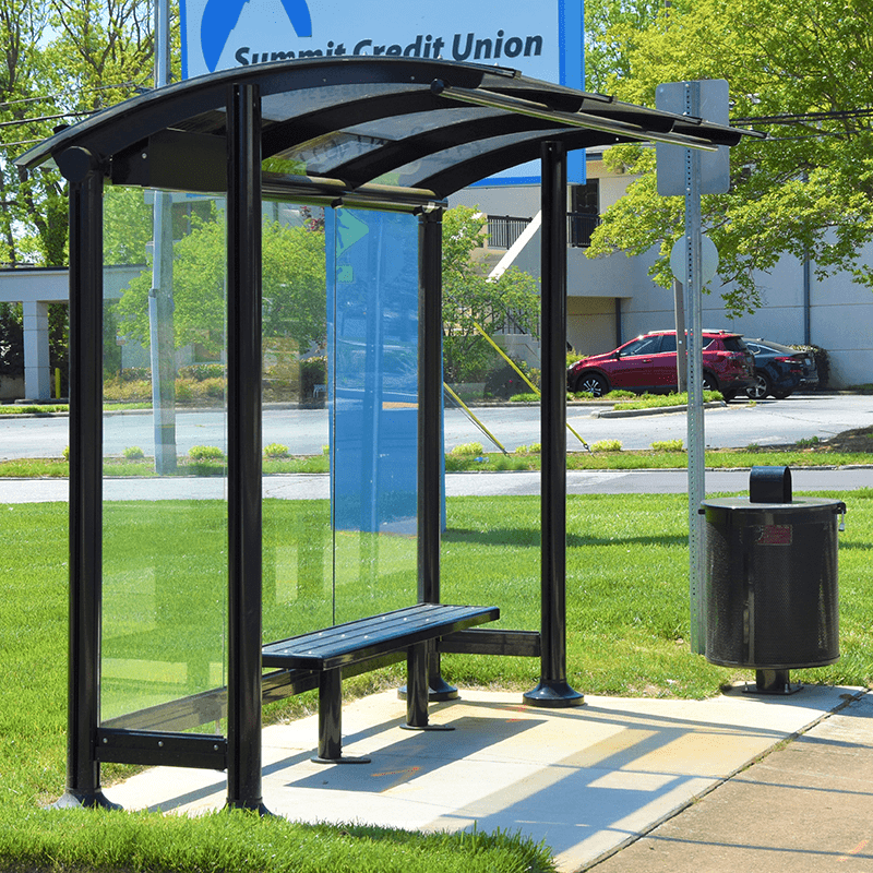 Right side view of a signa sunset bus shelter with glass sides, seating and a trash receptacle