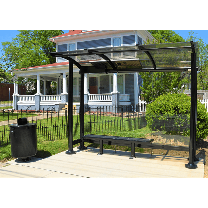 A black metal framed signa sunset bus shelter sits next to a blue home includes a glass siding, bench seating and a trash can