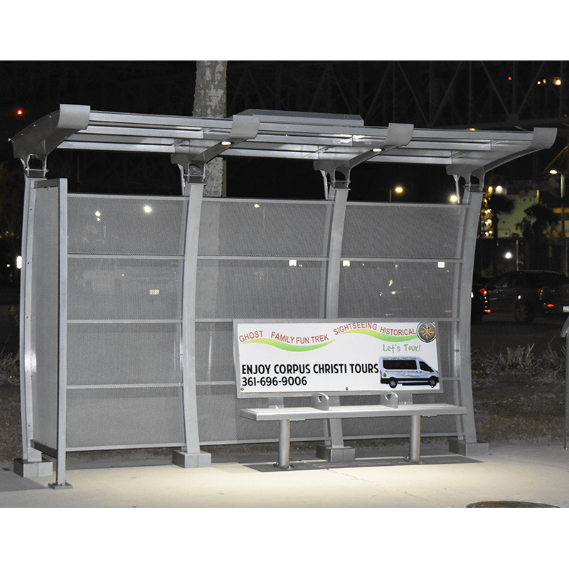 Right side view of a lit up bus shelter including a bench with back rest advertising