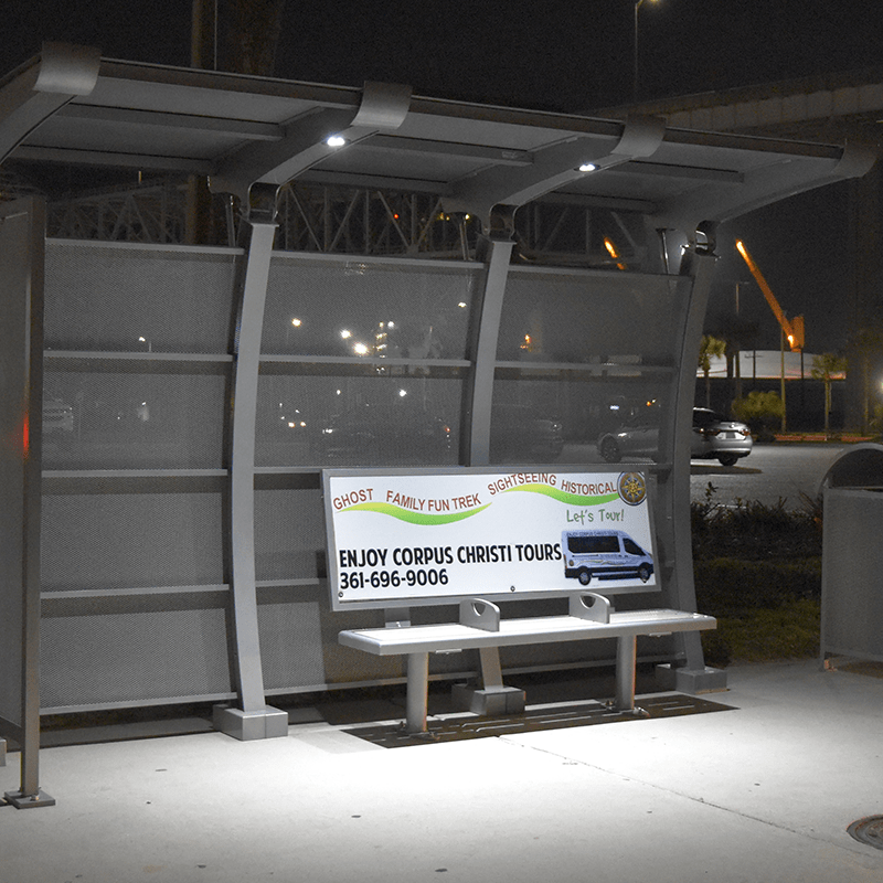 Bus shelter with bench advertising at night with lights highlighting advertisement
