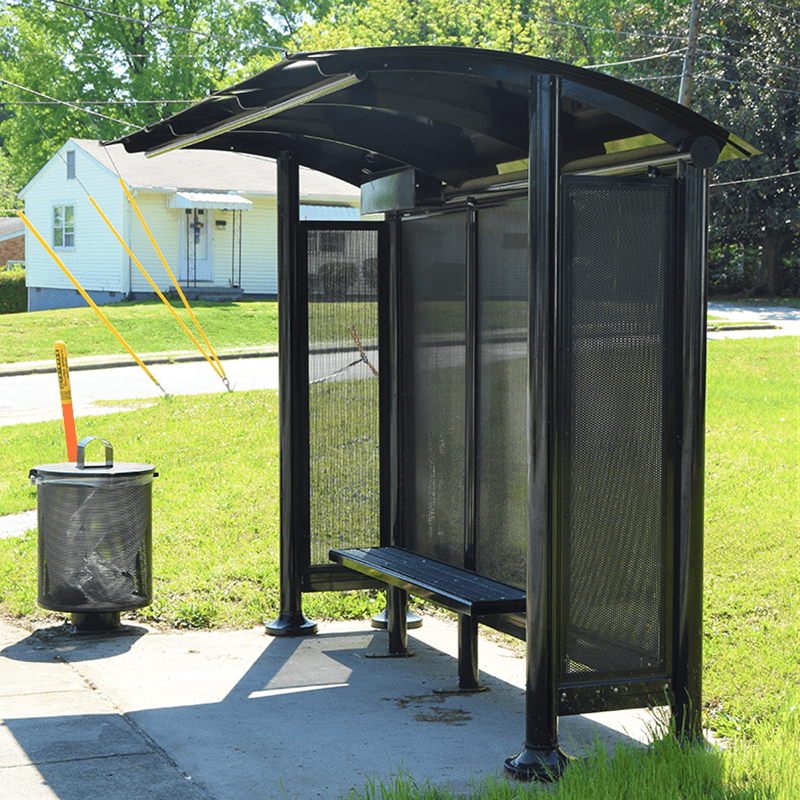 Left side of a signa sunset bus shelter with black siding, roof, bench and trash receptacle.