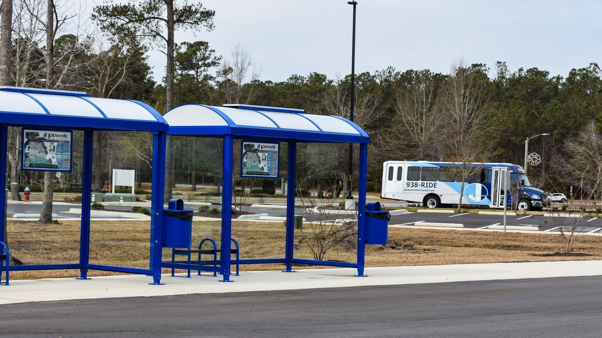 Two blue bus shelters with attached trash receptacles and seating and rider information displays