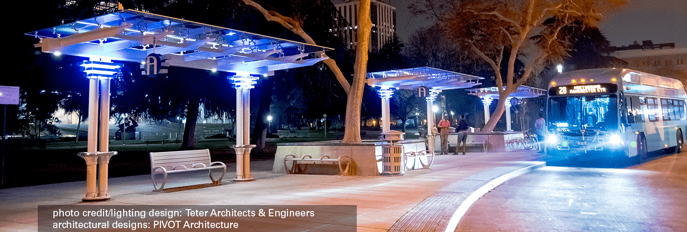 Multiple signature custom series bus shelters with full lighting at night, bench seating and trash receptacles as a bus awaiting passengers to load