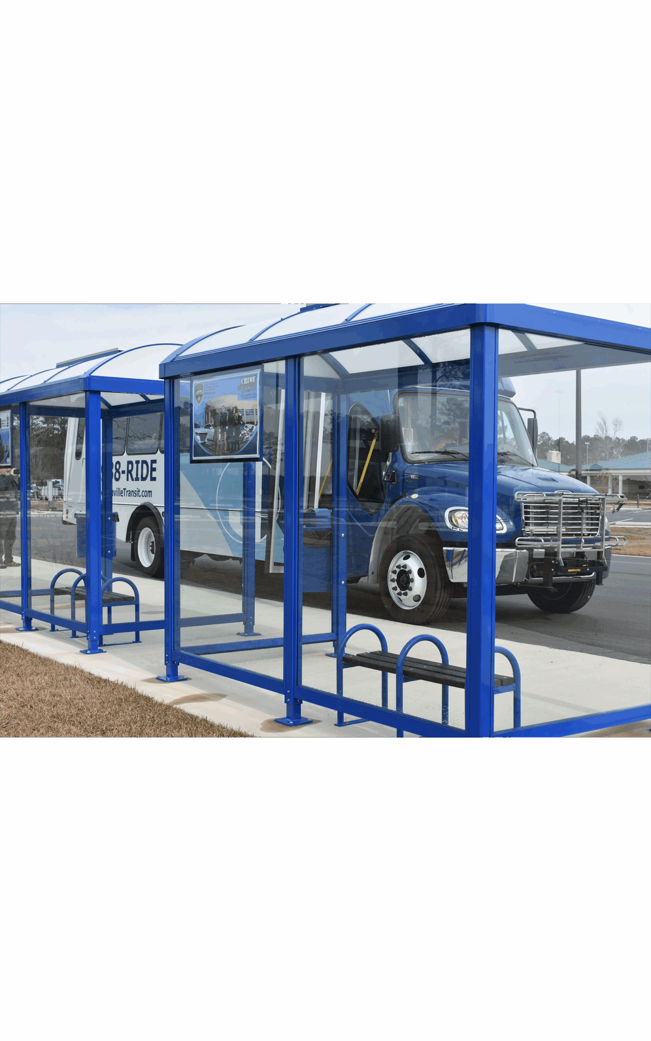 A back view of a Jacksonville bus shelter that has glass sides to view inside the shelter and see the benches and the bus on the other side
