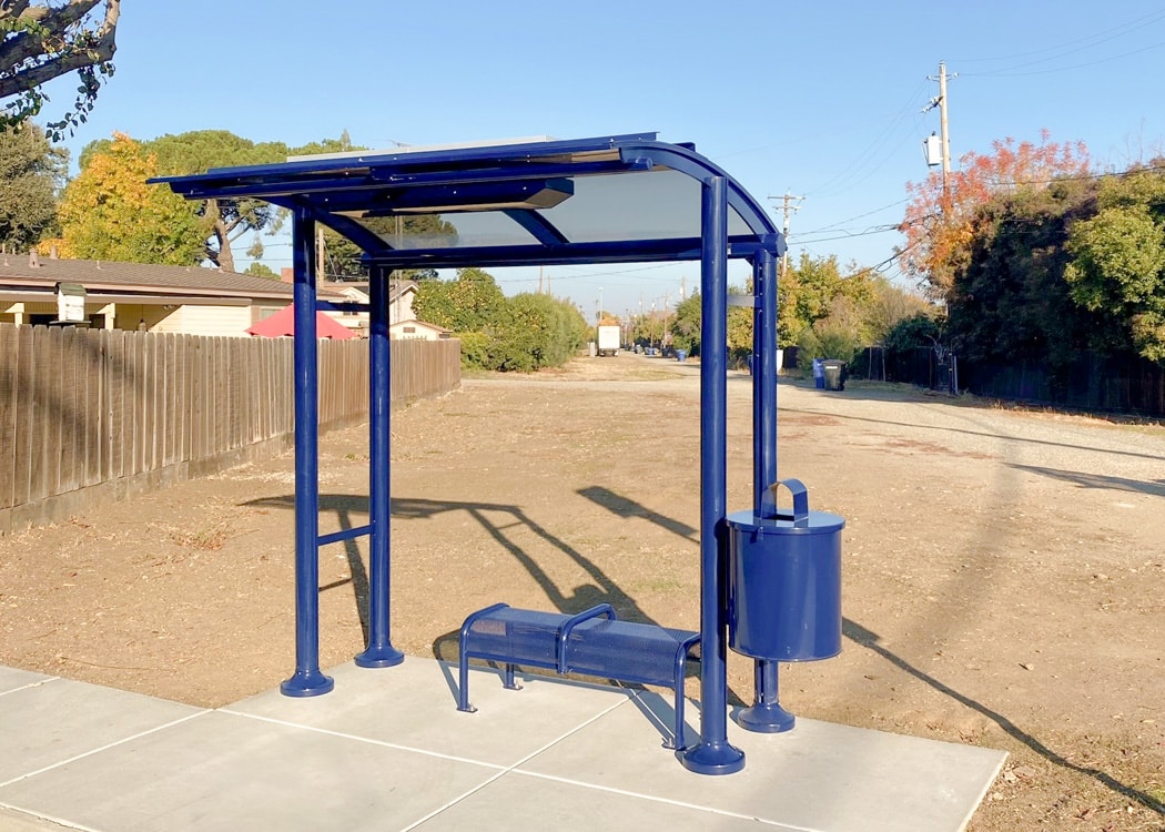 A blue bus shelter is seen from the front with bench seating for two and a trash receptacle
