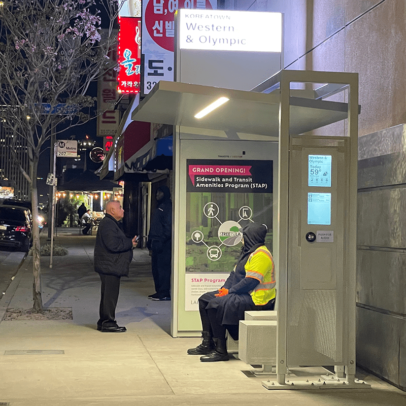 Evening picture of a Siga Custom bus shelter with passengers using its seating and viewing its rider information