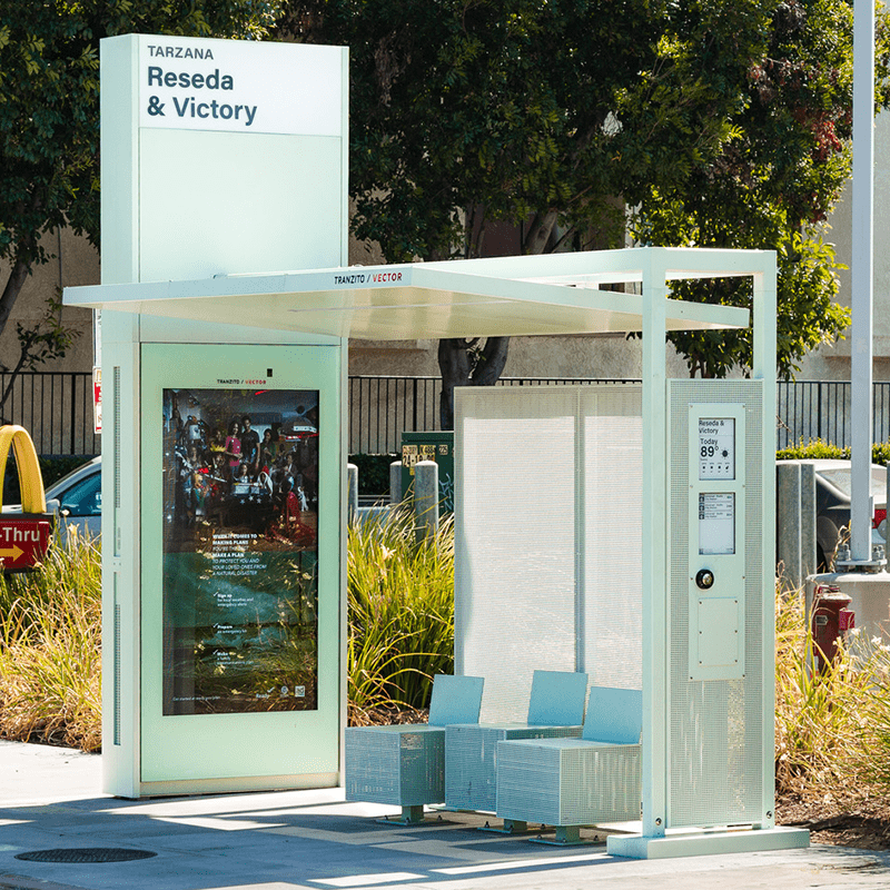 A Siga Custom bus shelter from the left side showing a digital display with route and temperature info and a side panel for advertising