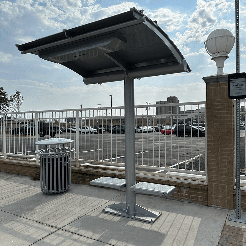 An Ecoshade is seen from the front right side with seats attached to the main ecoshade post and a trash receptacle on the left.