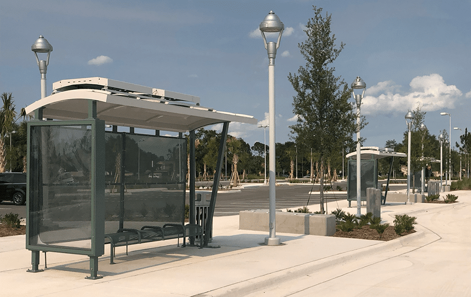 Three bus shelters are seen from a left side view at a transit center. Each has bench seating and green siding with a beige overhead.