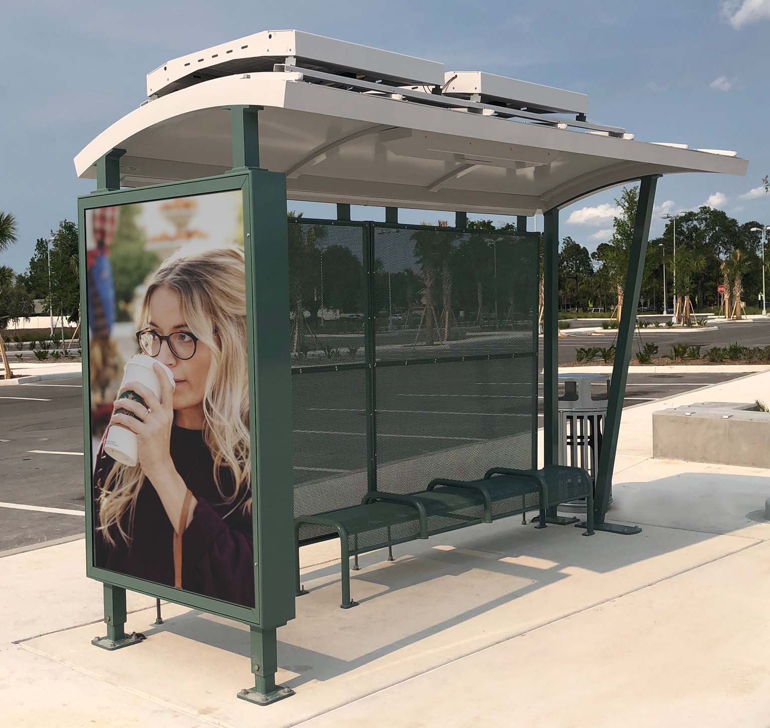 A siga custom bus shelter is seen from the left side to showcase the advertising display attached to the bus shelter with bench seating and a trash receptacle