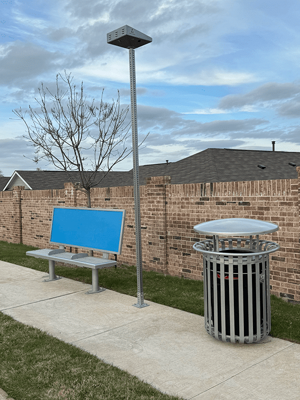 Left side view of a bench with advertising display features, a trash receptacle to the left and a light in between
