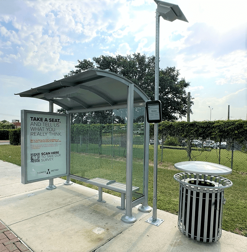 Left side view of a siga sunset bus shelter with advertising displays, a bench and trash receptacle