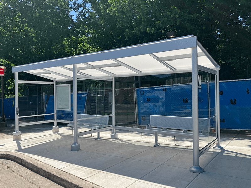 A large Signa Empire bus shelter is seen from the front right with two separated sections both with bench seating for three, full coverage and a display for routes on the back left wall.