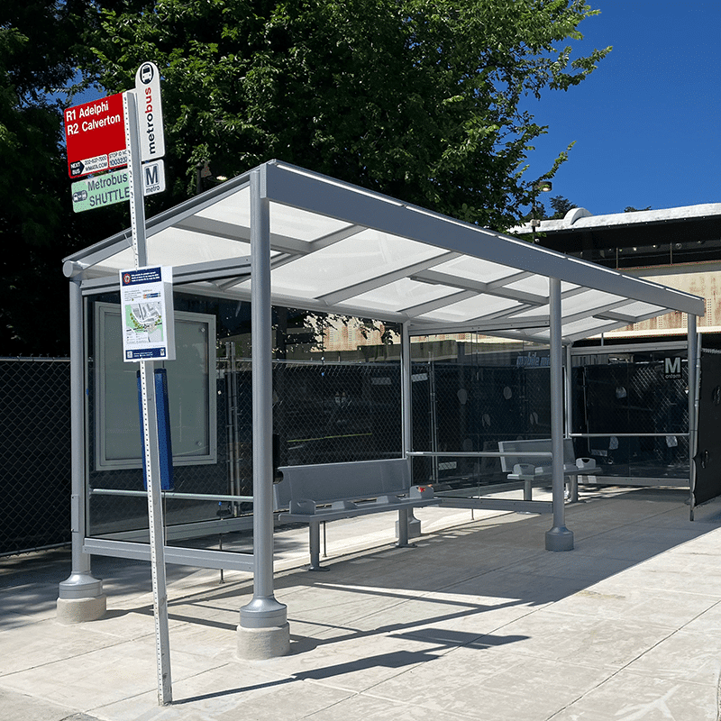 A Signa Empire bus shelter is seen from the front left with bench seating at two different benches and rider information displays.