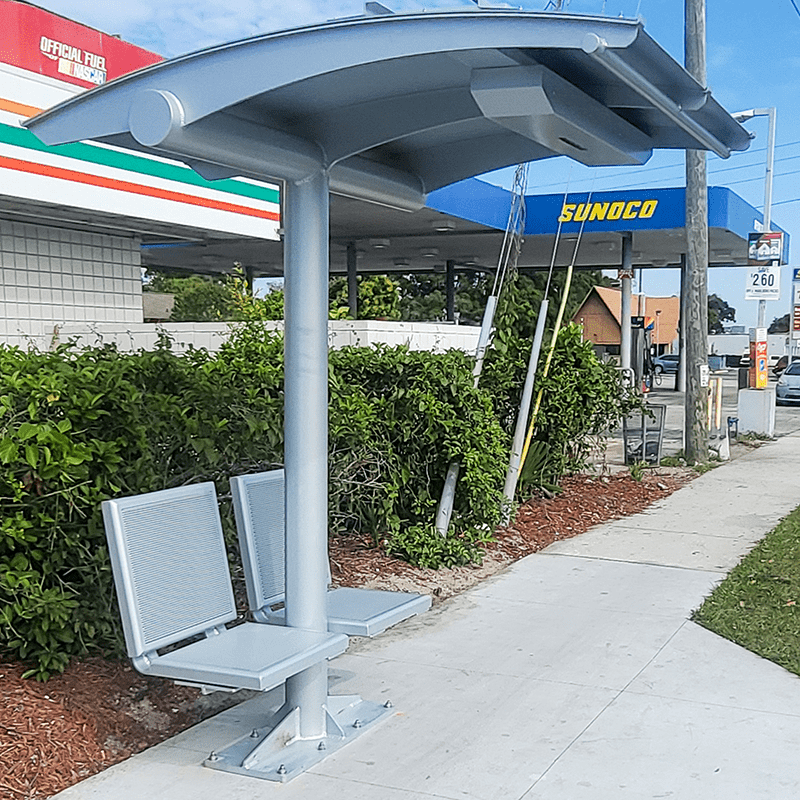 A signa sunset bus shelter is seen from the left side with two seats on either side of the shelter's post.