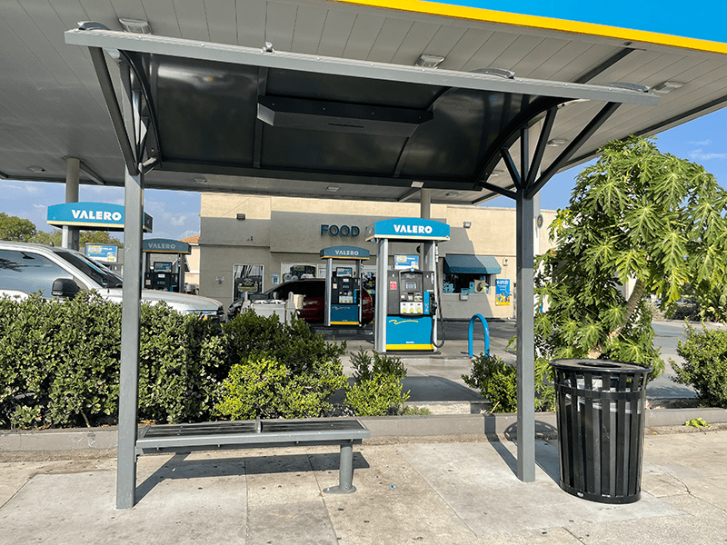A Signa Voyager bus shelter with a canopy top, bench seating and a trash receptacle close by