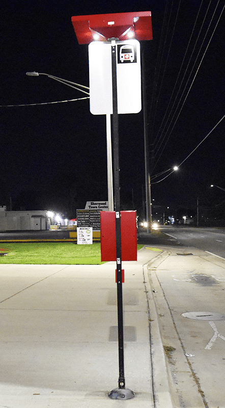 The back side of a bus stop sign post shows the lit post from the top and the rider display piece attached to the post.