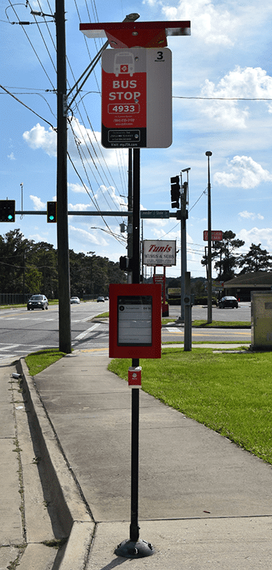 A bus stop sign is seen from the front with a bus stop information sign on top, bus rider information in the middle and a info button below.