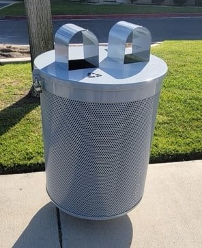 A trash receptacle is seen from the front with two arched openings, once of which is for recyclables indicated by the recycling logo.