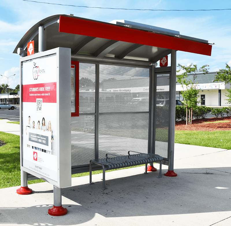 A siga sunset bus shelter is seen from the front left with a left side advertisement display and a bench with seating for three on the right of the shelter.
