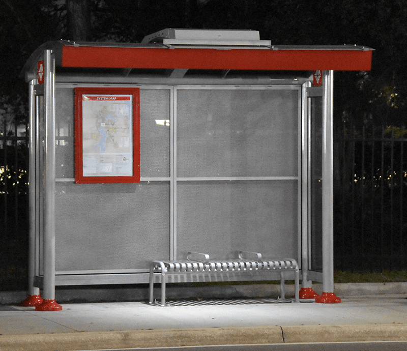 A signa sunset bus shelter is seen from the front with a rider display on the back left panel and a bench with seating for three on the right.